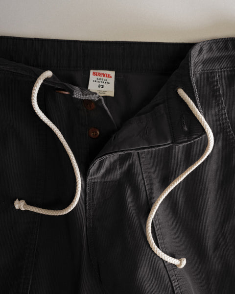 Close-up of dark charcoal Classic Corduroy Pants - Charcoal, featuring a white drawstring, button fly, and interior size 32 brand label.