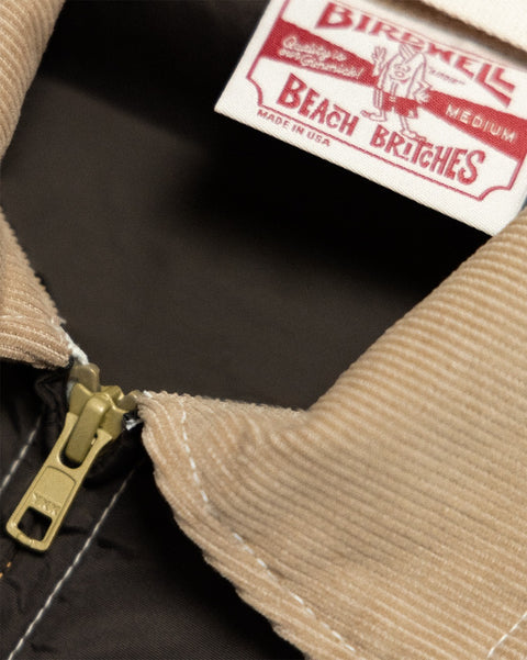 Close-up of a brown/acorn Capistrano Jacket featuring a tan corduroy collar, a brass zipper, and a brand label at the neckline.