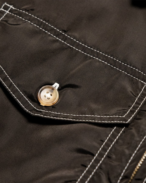 Close-up of a brown Capistrano Jacket - Brown/Acorn pocket flap featuring white contrast stitching and a light-colored button.