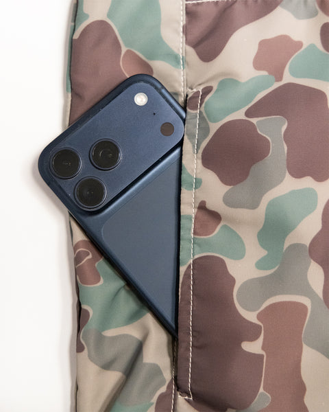 A dark blue smartphone partially tucked into the pocket of a camouflage-patterned Capistrano Jacket - Frogskin/Acorn.