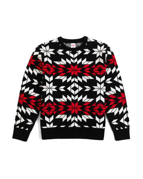 The North Pole Sweater is a black acrylic sweater with a bold geometric snowflake pattern in white and red on the chest, sleeves, and torso—perfect for festive winter celebrations.