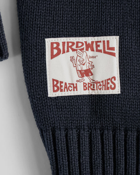A close-up of the Racing Cardigan Sweater in navy/bone, a men's knit made from 100% cotton, featuring a white patch label with 