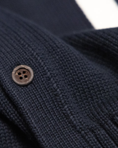 Close-up of the Racing Cardigan Sweater - Navy/Bone, showing a brown four-hole button on 100% cotton knit. The men's sweater's textured navy material and stylish design are clearly visible.