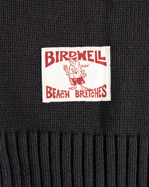A close-up of a black knit cotton sweater with a white patch reading 