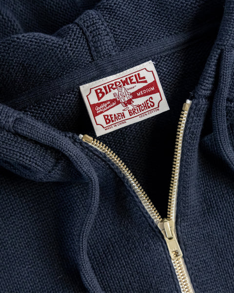 Close-up of the Comp Zip Sweater - Navy/Bone, highlighting a white and red Birwell Beach Britches label above a partially unzipped gold YKK Vislon zipper, showcasing the premium details of this cotton zip-up hoodie.