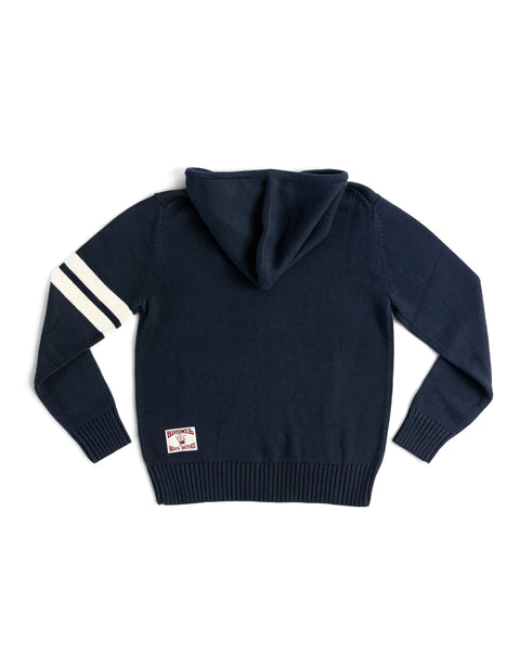 The Comp Zip Sweater - Navy/Bone features two white stripes on the left sleeve, a small rectangular back patch near the hem, and a premium YKK Vislon zipper. The cotton sweater is shown laid flat on a white background.