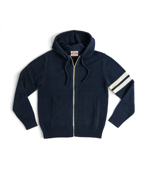 The Comp Zip Sweater - Navy/Bone is a cotton hoodie with a hood, ribbed hem and cuffs, two front pockets, and two white stripes on the right sleeve. It features a YKK Vislon front zipper for durability.