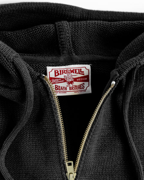 Close-up of the Comp Zip Sweater - Black/Gray with the zipper partially open, showing a white and red Birdwell Beach Britches tag indicating it's 100% cotton and made in China.