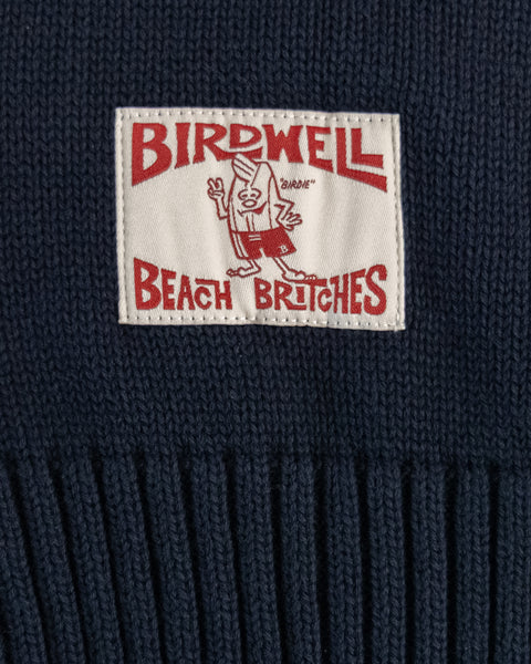 A rectangular patch with red text and a cartoon character reads Birdwell Beach Britches on the navy/bone Comp Stripe Sweater's durable knit background.