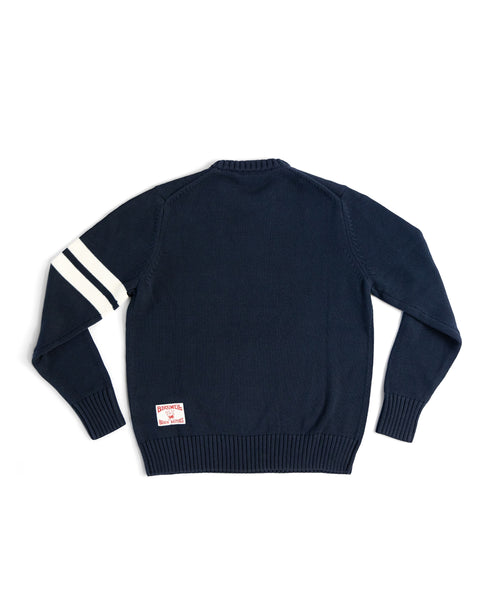 The Comp Stripe Sweater - Navy/Bone is made from 100% cotton, with two bone stripes on the left sleeve and a rectangular patch near the lower back hem, shown laid flat on a white background.