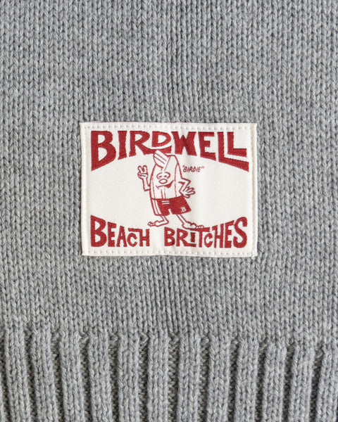 A close-up of the Comp Stripe Sweater - Gray/Navy, a gray cotton-blend sweater with a white patch reading 