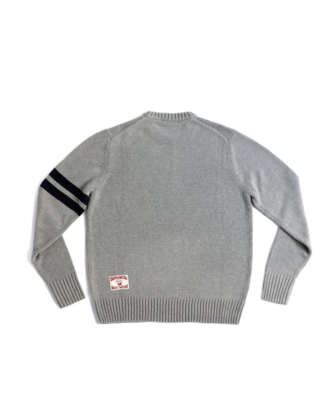 The Comp Stripe Sweater - Gray/Navy is shown from the back, with two black horizontal stripes on the left sleeve and a white rectangular patch with red text near the bottom hem.