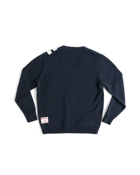 The Racing Cardigan Sweater - Navy/Bone is a men's 100% cotton knit, shown from the back with two white stripes on the left shoulder and a white rectangular label with red text near the bottom hem.
