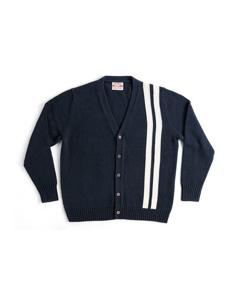 The Racing Cardigan Sweater - Navy/Bone is a men's 100% cotton knit, featuring a V-neck, button-up front, and two vertical white stripes on the left shoulder and chest, laid flat on a white background.