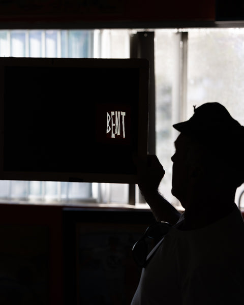 A silhouette wearing the BENT Comp Jacket - Black holds a dark board with 
