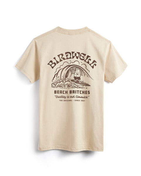 The Surfin Birdie T-Shirt - Sand is a heavyweight beige cotton tee with a back graphic of a Travis Price surfer beneath “BIRDWELL,” plus “BEACH BRITCHES,” “Quality is our gimmick,” and “THE ORIGINAL – SINCE 1961” in brown.