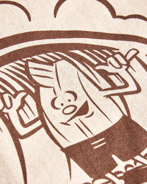 The Surfin Birdie T-Shirt - Sand features a brown line drawing of a smiling cartoon banana with raised arms and an expressive face, printed on beige cotton heavyweight fabric. The playful design is inspired by Travis Price for Birdwell.