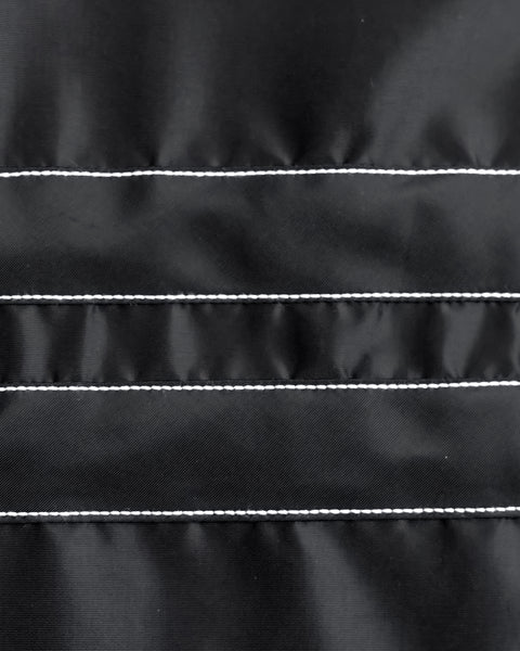 Close-up of black fabric with horizontal parallel white stitching lines gives the BENT Comp Jacket - Black a quilted look. The surface appears smooth and slightly shiny.